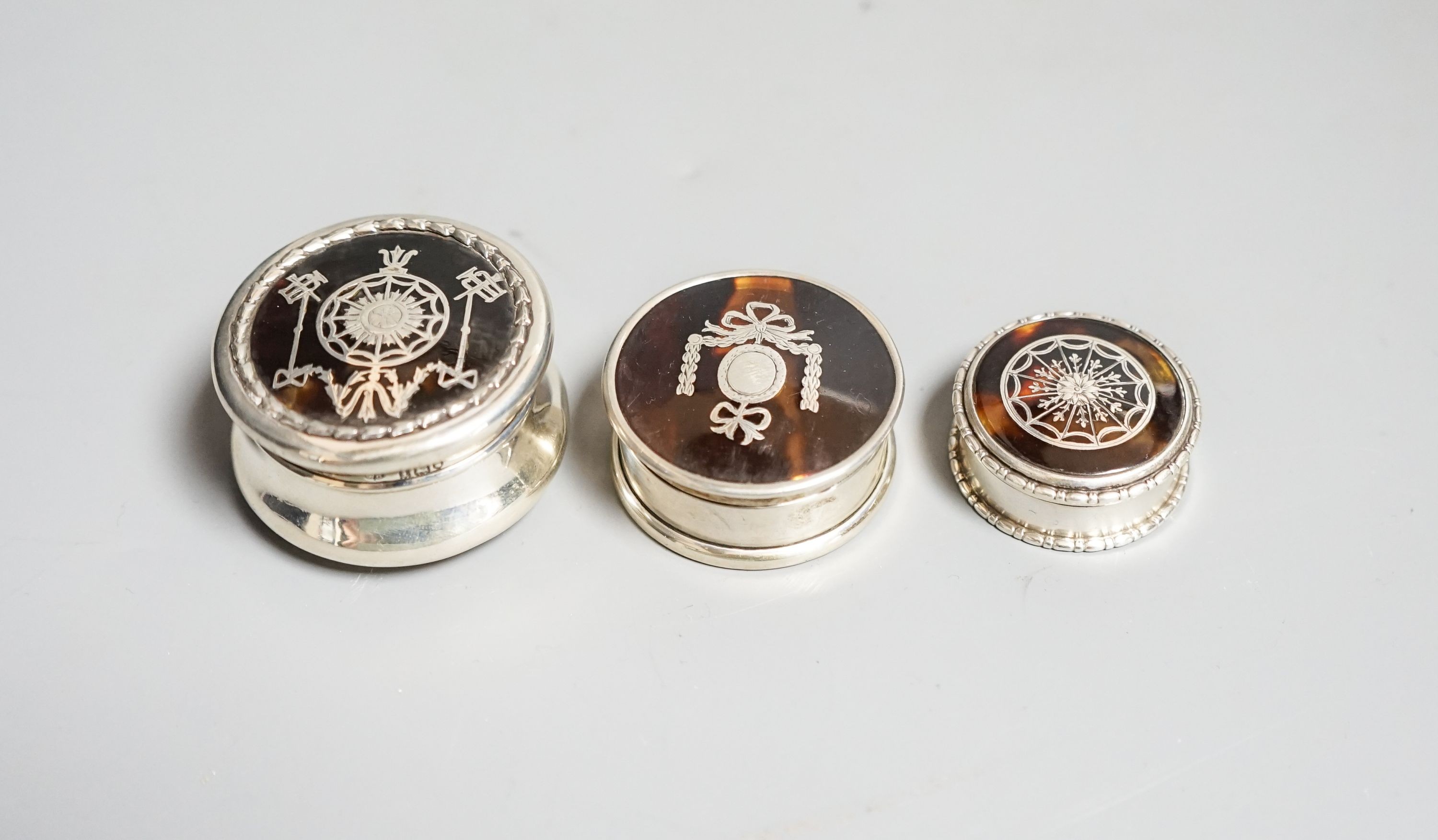 Three assorted early 20th century small silver and tortoiseshell pique circular boxes and covers, largest by William Comyns, 46mm.